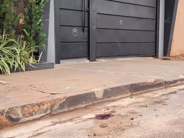 Sangue da vítima no chão e marcas de tiros no portão; Foto: Campo Grande News